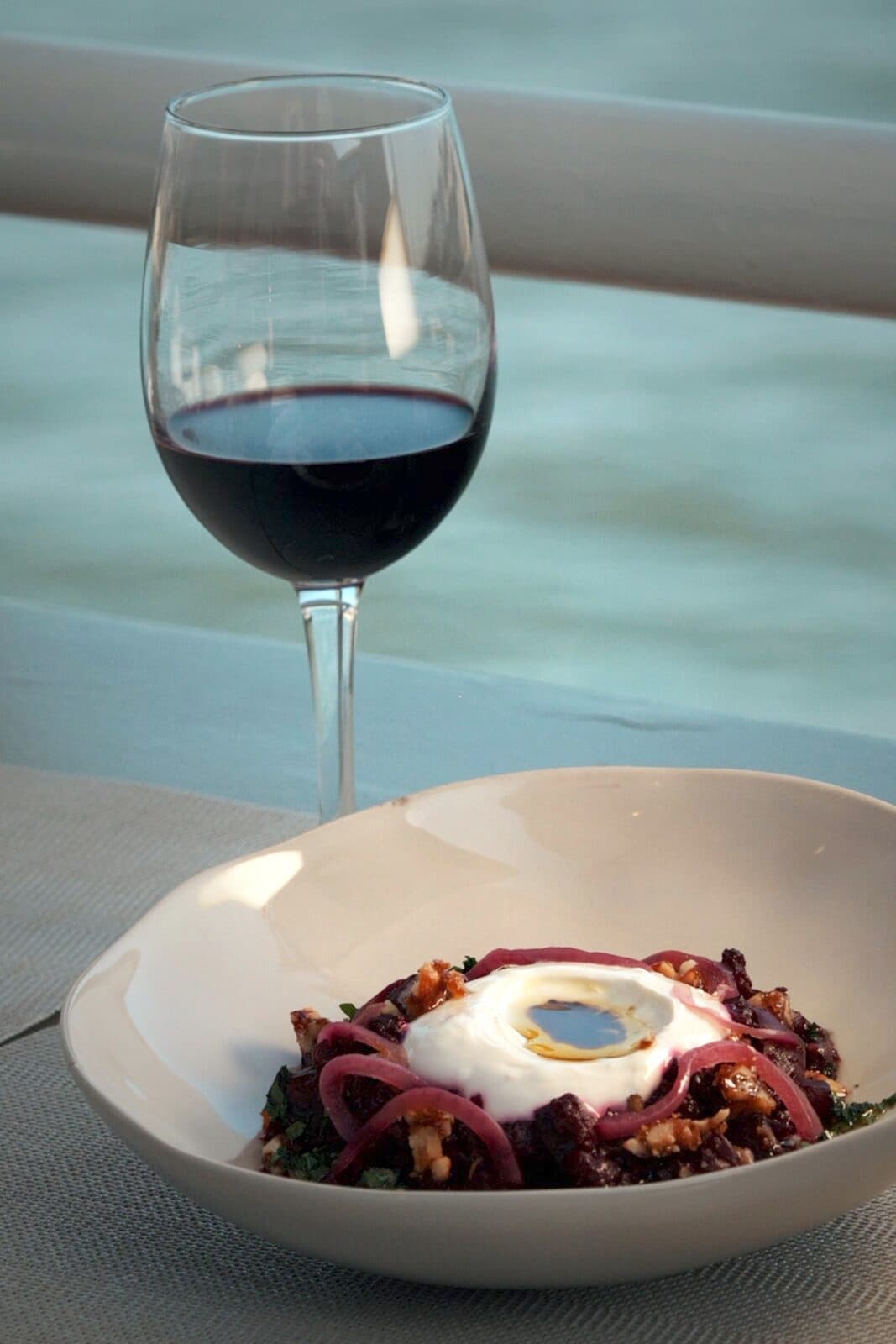A glass of red wine beside a bowl of grains and a soft egg, on the terrace at TEJÁ.