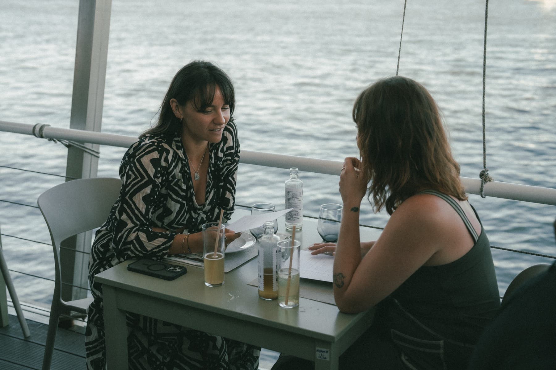 Two people working at a table over the water at TEJÁ, papers and drinks between them.
