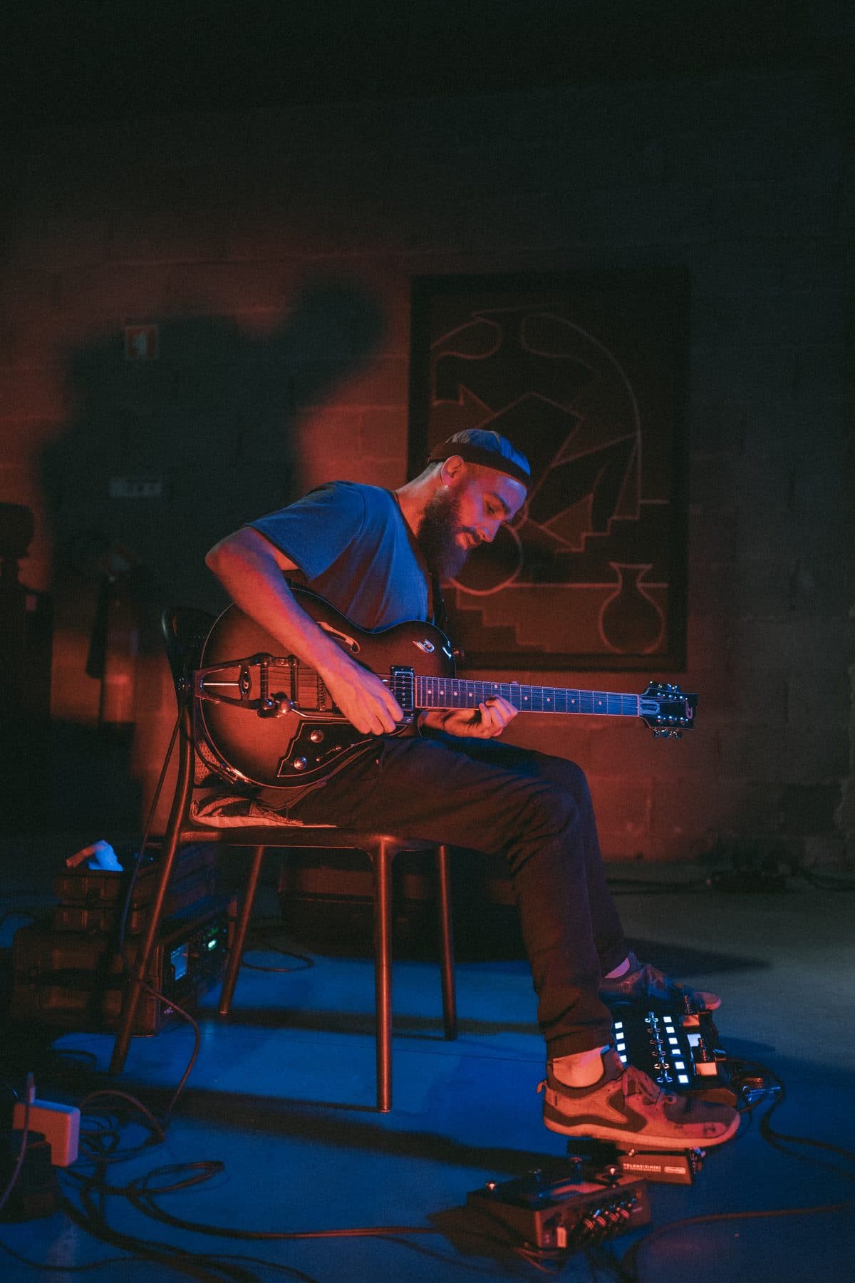 A guitarist playing in the brick hall at TEJÁ, lit red and blue.